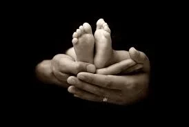 Mains d'adulte tenant avec douceur les petits pieds d'un bébé sur fond noir
