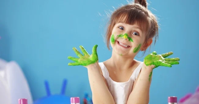 Enfant souriante avec des mains et des taches de peinture verte sur le visage, activité de peinture créative