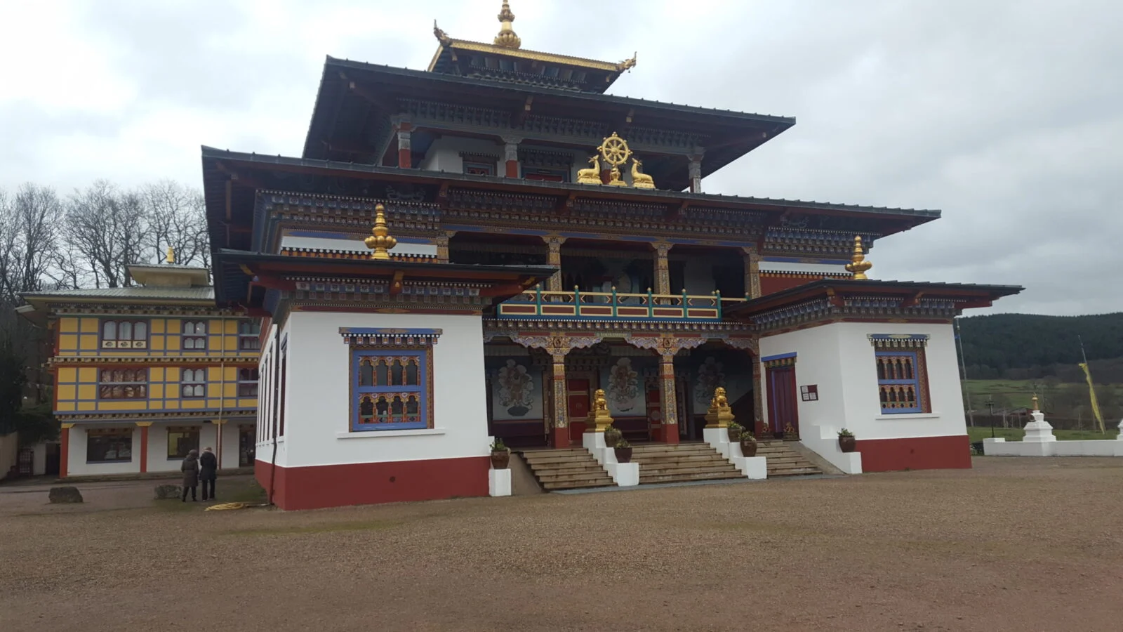 Temple bouddhiste traditionnel avec ornementations dorées et architecture typique entouré d'un paysage boisé sous un ciel nuageux
