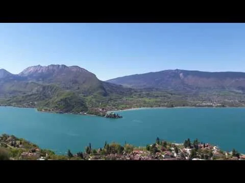 Vue panoramique du lac d'Annecy entouré de montagnes verdoyantes sous un ciel bleu ensoleillé