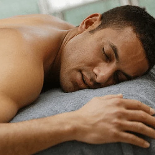 Homme allongé sur le ventre, détendu, yeux fermés, atmosphère de relaxation et bien-être.