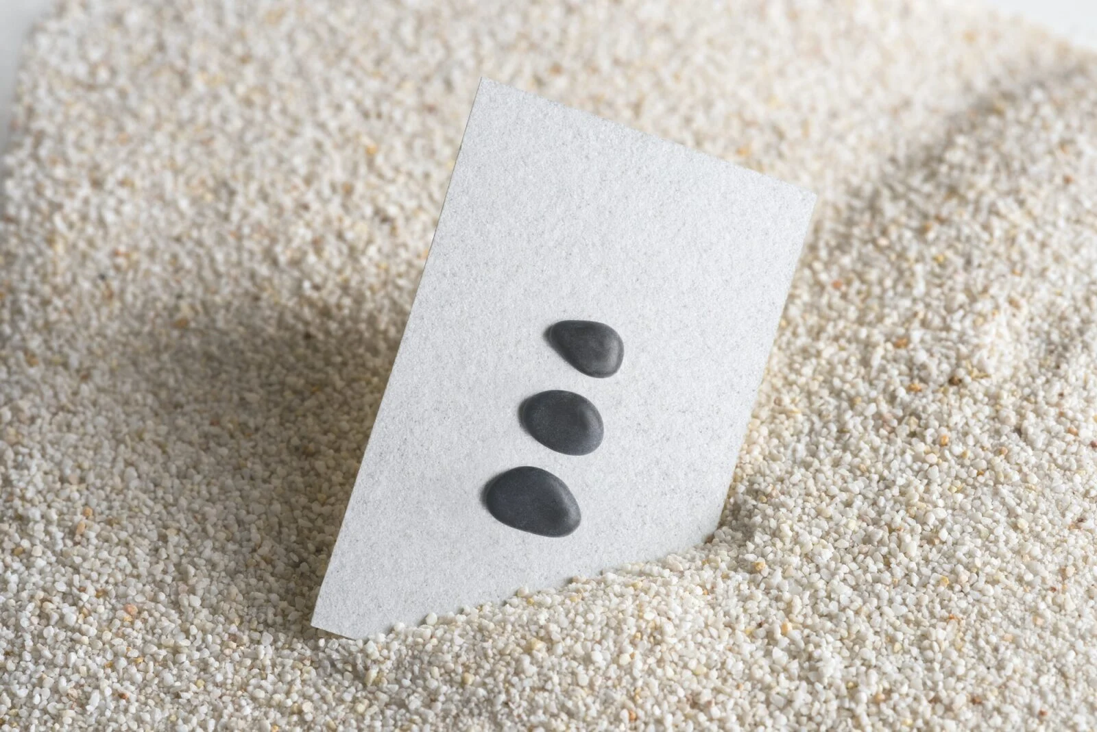 Carte blanche avec trois pierres noires sur fond de sable