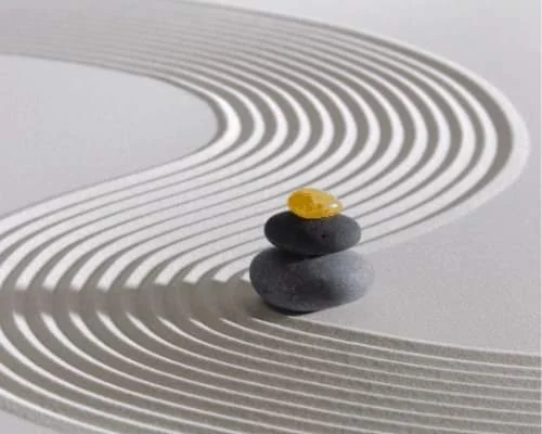 Jardin zen avec galets empilés et motifs ondulés sur le sable.