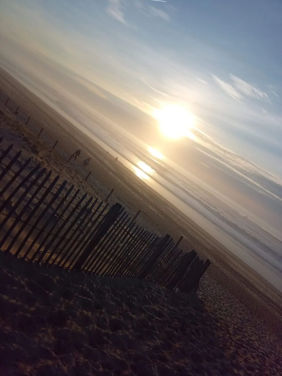 Coucher de soleil sur une plage avec clôture en bois et promeneurs.