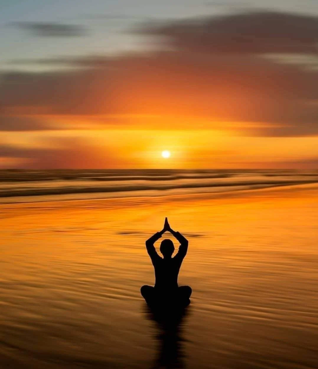 Silhouette pratiquant la méditation sur une plage au coucher du soleil.