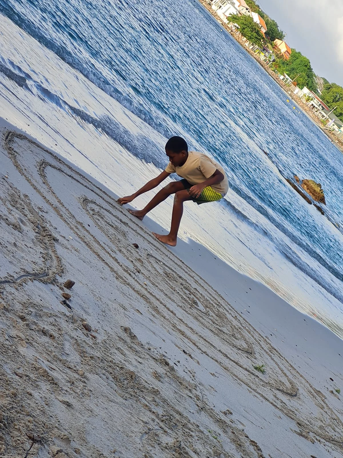 Enfant dessinant dans le sable sur une plage près de la mer. Martinique
