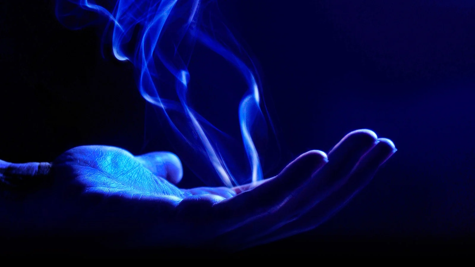 Main illuminée tenant de la fumée dans une lumière bleue.